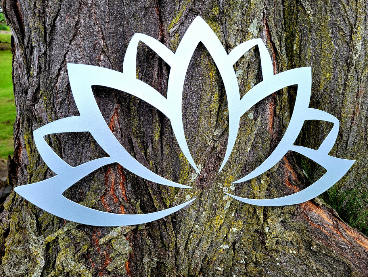Silver metal lotus flower design sitting against a large tree trunk.