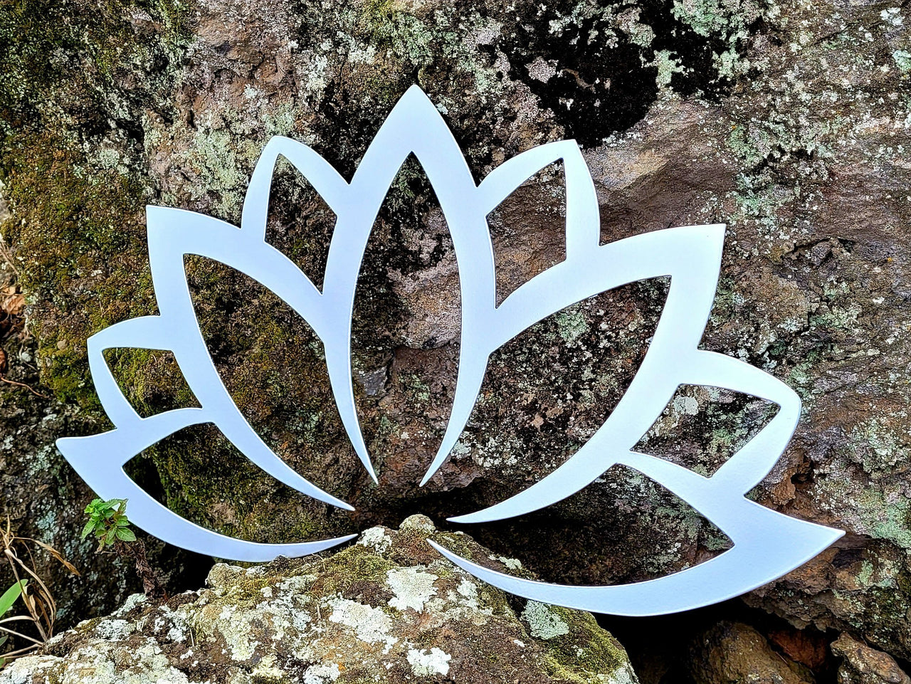 Silver metal lotus flower design sitting against a moss covered rock background.