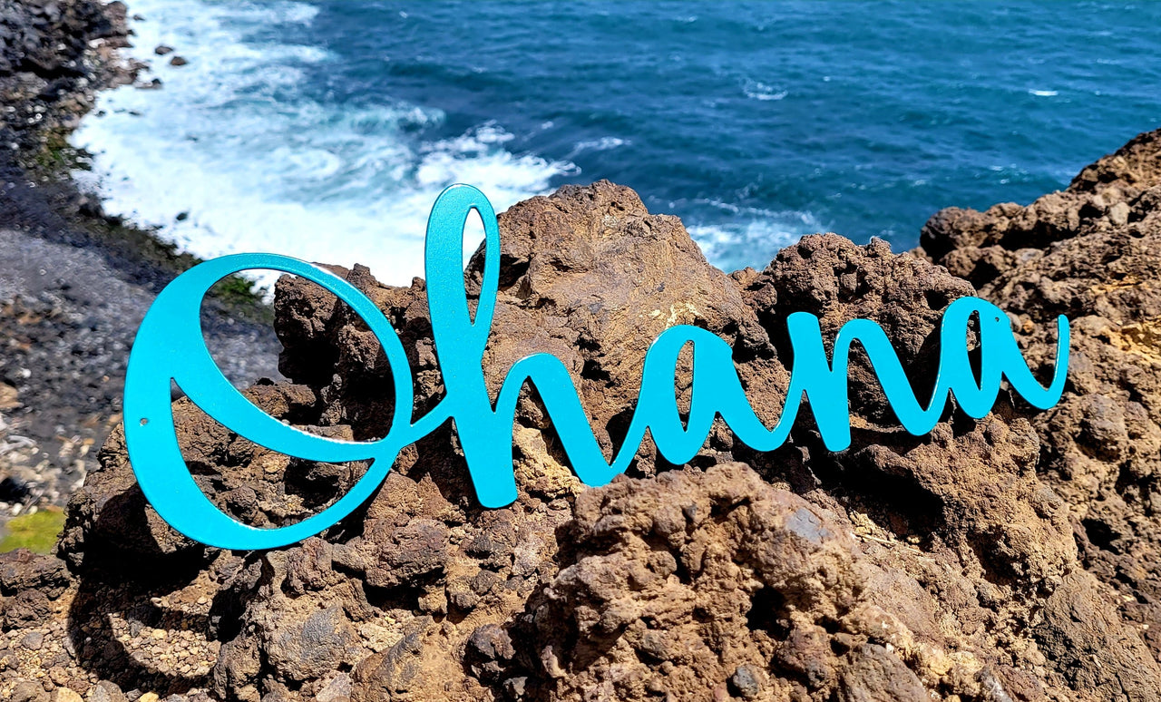 Turquoise metal ohana script word sitting on a lava cliffside with a rocky Hawaiian beach in the background